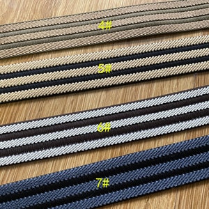 May include: Four different types of striped elastic trim, each with a different color combination. The trim is arranged in a row from top to bottom, with the top trim being beige and brown, the second trim being black and beige, the third trim being brown and white, and the bottom trim being navy blue and black. Each trim is labeled with a number, starting with 4# and ending with 7#.