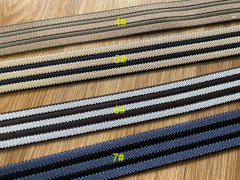 May include: Four different types of striped elastic trim, each with a different color combination. The trim is arranged in a row from top to bottom, with the top trim being beige and brown, the second trim being black and beige, the third trim being brown and white, and the bottom trim being navy blue and black. Each trim is labeled with a number, starting with 4# and ending with 7#.