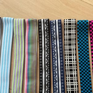 Op de afbeelding: Een verzameling elastische banden in verschillende patronen en kleuren. Ontwerpen omvatten zwart-witte strepen, blauwe strepen, groen-paarse strepen, een regenboogpatroon en zwart-witte geometrische vormen.