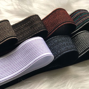 Könnte beinhalten: Sechs Rollen elastischer Besatz mit glitzerndem Finish. Der Besatz ist schwarz mit gold, rot mit gold, schwarz mit silber, weiß mit lila, schwarz mit blau und schwarz mit Regenbogen-Glitter.