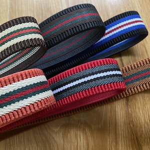 May include: Five different striped elastic bands in various colours, including brown, red, black, and blue. The bands have a ribbed texture and are arranged in a pile.