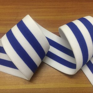 May include: White elastic band with blue stripes. The band is folded in half and the stripes are visible on both sides.
