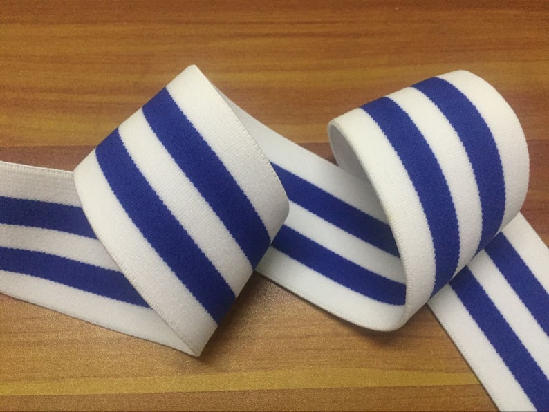 May include: White elastic band with blue stripes. The band is folded in half and the stripes are visible on both sides.