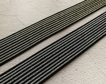 May include: Two black elastic bands with gold and silver stripes. The bands are lying on a white textured surface.