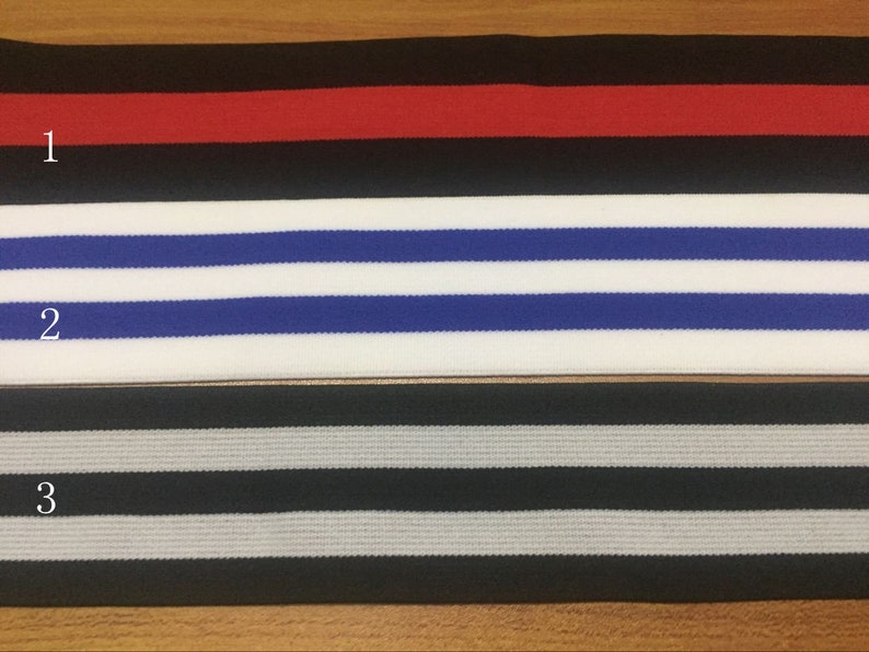 May include: Three different types of elastic trim with striped patterns. The first trim is black with a red stripe. The second trim is white with blue stripes. The third trim is black with gray stripes.