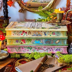 May include: Three vintage hardcover books with colorful illustrations and whimsical designs. The books are stacked on top of each other and have a magical, fairytale theme. The books are surrounded by greenery and candles, creating a cozy and enchanting atmosphere.