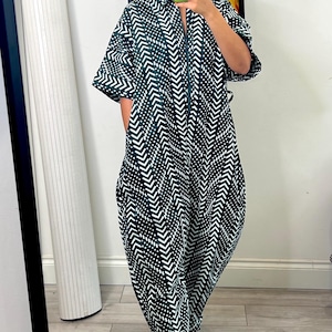 May include: A dark green and white jumpsuit featuring a repeating chevron and dot pattern. The garment has short sleeves, a collared neckline, and a front zipper closure. The legs are loose-fitting and taper slightly toward the hem at the ankles.