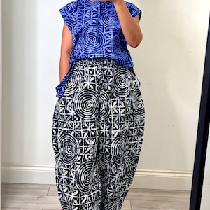 Puede incluir: Una blusa azul sin mangas con un patrón circular y geométrico blanco, combinada con pantalones holgados en blanco y negro con un estampado circular y geométrico a juego. Los pantalones tienen una cintura elástica con cordón.