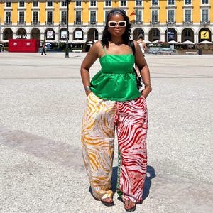 May include: A bright green satin camisole top with thin straps paired with loose-fitting trousers featuring a split-leg design. The left leg has a yellow and white zebra print, while the right leg features a red and white zebra print pattern.