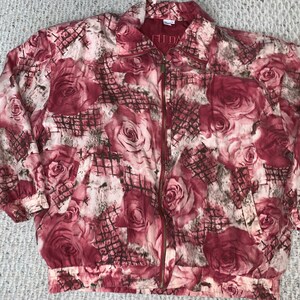 May include: A zip-up jacket with a rose pattern in shades of burgundy, cream, and gray. The jacket has a collared neckline, elastic cuffs, and a matching elastic waistband. The fabric features a grid-like overlay. The text "FU DA" is visible on the collar.