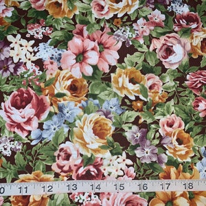 May include: A brown fabric with a floral pattern featuring pink, yellow, and purple roses. The fabric is measured with a ruler in inches.
