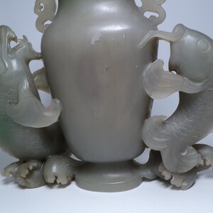 May include: A gray jade vase with two dragon handles. The vase is carved with intricate details and has a smooth, polished finish.