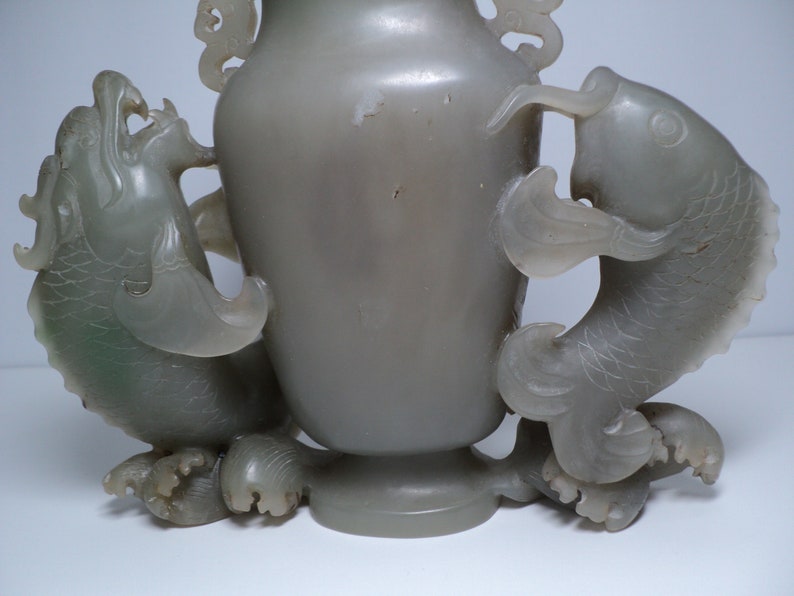 May include: A gray jade vase with two dragon handles. The vase is carved with intricate details and has a smooth, polished finish.