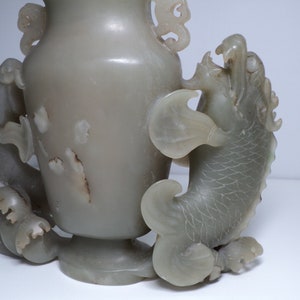 May include: A pale green jade vase with two dragon-like handles. The vase is carved with intricate details and has a smooth, polished finish.