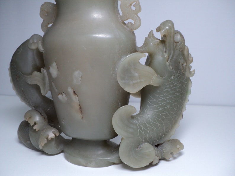 May include: A pale green jade vase with two dragon-like handles. The vase is carved with intricate details and has a smooth, polished finish.