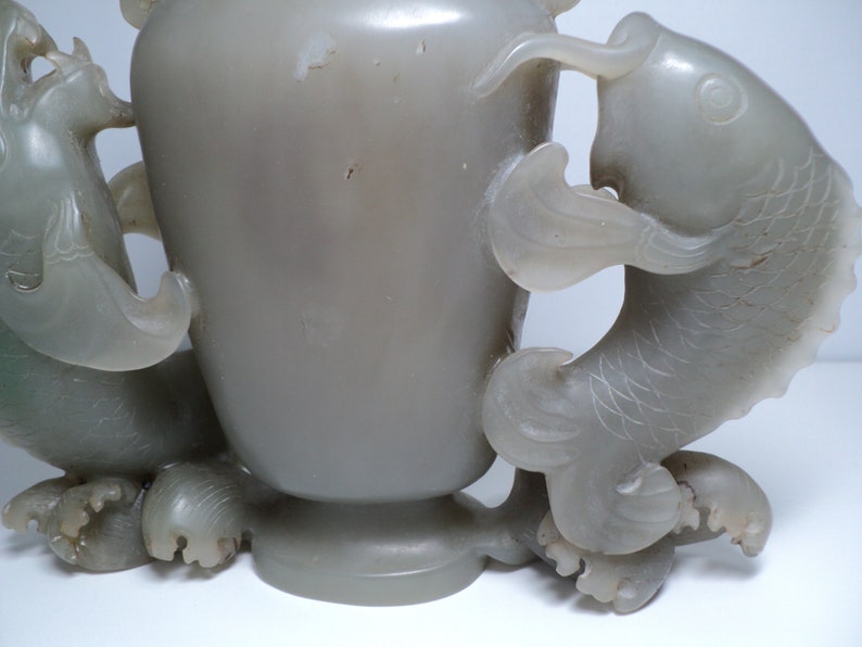 May include: A gray jade vase with two dragon handles. The vase is carved with intricate details and has a smooth, polished finish.