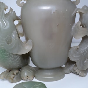 May include: A pale green jade vase with two fish handles. The vase is carved with intricate details and has a smooth, polished finish.