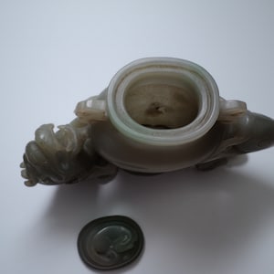 May include: A jade green carved vase with a lid, shaped like a mythical creature. The vase is decorated with intricate details and has a smooth, polished finish.