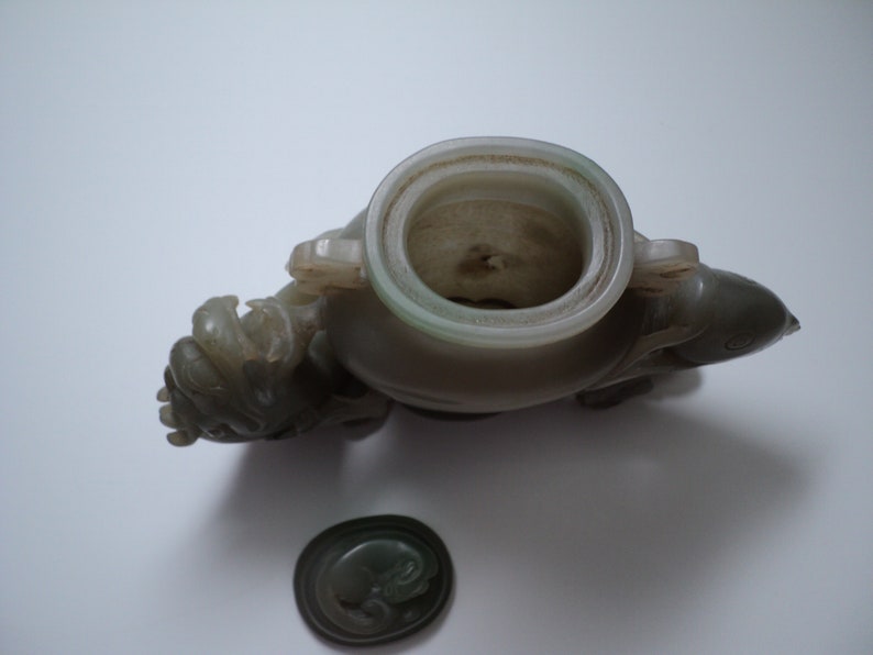 May include: A jade green carved vase with a lid, shaped like a mythical creature. The vase is decorated with intricate details and has a smooth, polished finish.