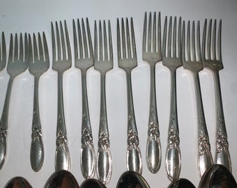 May include: A set of silver forks with an ornate floral design on the handle. The forks are arranged in a row on a white surface.