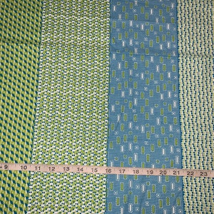 May include: Four fabric swatches with different geometric patterns in green, blue, and white. The swatches are lined up side by side and measured with a ruler.