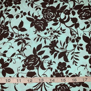 May include: A teal fabric with a brown floral pattern. The fabric features a repeating pattern of roses and leaves. A measuring tape is visible at the bottom of the image.