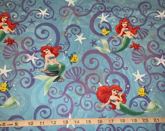 May include: A blue fabric with a repeating pattern of Ariel the Little Mermaid, seashells, starfish, and fish. The fabric has a purple swirl design.
