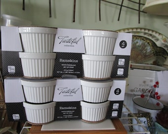 May include: A set of four white porcelain ramekins, each with a fluted design. The ramekins are packaged in a black and white box with the text "Tasteful collection" and "Ramekins" printed on it. The box also includes the text "4 pc" and "White Porcelain Set of Four".