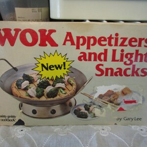 May include: A cookbook cover with a red title "WOK Appetizers and Light Snacks" with a yellow starburst that says "New!" and a picture of a wok with food inside.