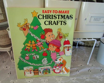 May include: A green book with the title "EASY-TO-MAKE CHRISTMAS CRAFTS" on the cover. The cover features a cartoon illustration of a Christmas tree decorated with ornaments, a Santa Claus, a reindeer, and other festive characters.