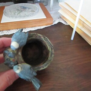 May include: A ceramic birdhouse with a brown and green exterior. Two blue birds are perched on the edge of the birdhouse.