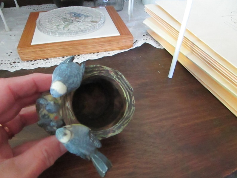 May include: A ceramic birdhouse with a brown and green exterior. Two blue birds are perched on the edge of the birdhouse.