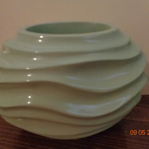 May include: A light green ceramic vase with a wavy, textured design. The vase is round and has a wide opening.