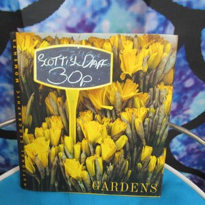 May include: A book cover featuring a close-up of yellow daffodils with a sign that reads "Scottish Daff 30p". The book title is "Gardens" and the National Geographic Moments logo is visible on the spine.