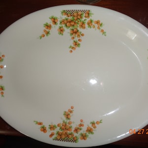 May include: A white oval serving platter with a floral design featuring orange and green berries. The platter has a scalloped edge and a smooth, glossy finish.