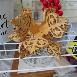May include: A wooden, intricately carved, multi-layered, star-shaped ornament. The ornament is light brown and has a delicate, intricate design.