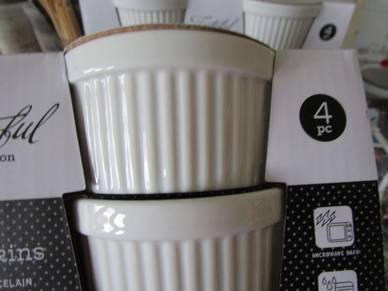 K&ouml;nnte beinhalten: Set mit vier wei&szlig;en Keramik-Ramekins mit geripptem Design. Die Ramekins sind mikrowellengeeignet und werden in einer Schachtel mit schwarz-wei&szlig;em Punkte-Muster verpackt. Die Schachtel enth&auml;lt auch den Text "4 pc" und "Microwave Safe".