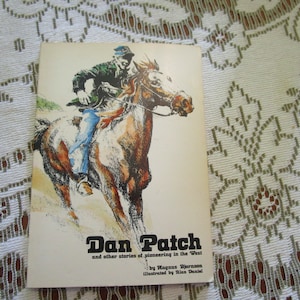 May include: A vintage book cover featuring a black and white illustration of a cowboy riding a horse. The title of the book is "Dan Patch and other stories of pioneering in the West".