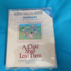 May include: A cassette tape with a beige label featuring a colorful illustration of children playing in a field. The text on the label reads "A Child Shall Lead Them" and "Lessons in Hope From Children With Cancer".