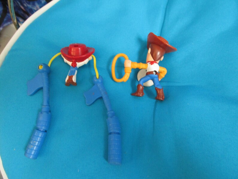 May include: A set of three blue plastic toy figures, including Woody from Toy Story, with a yellow lasso and a red hat. The figures are on a blue surface.