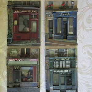 May include: Four rectangular decorative plaques depicting French storefronts. The plaques feature detailed facades with text such as "Vins de Bourgogne", "Livres", "France-Soir", and "Restaurant 62". Each plaque has a unique color scheme and architectural style.