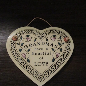 May include: A heart-shaped ceramic plaque with a black and white border and floral designs. The plaque reads "Grandmas have a Heartful of Love".