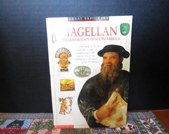 May include: A softcover book titled Great Explorers: Magellan and the Exploration of South America. The cover features a portrait of a bearded man in a dark hat, historical illustrations of artifacts, a ship, and the Scholastic logo at the bottom.