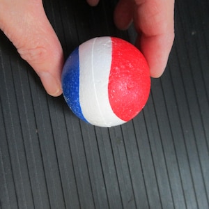 May include: A white ball with red and blue stripes. The ball is made of foam and has a textured surface.