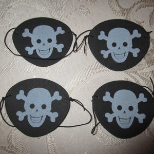 May include: Four black pirate eye patches with a light blue skull and crossbones design. Each patch has a string attached for securing it to the face. The eye patches are oval-shaped and suitable for costume parties.