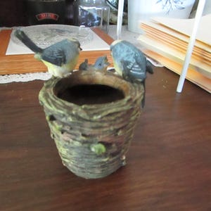 May include: A small ceramic birdhouse planter with a brown bark-like exterior and a green leafy accent. Four blue birds are perched on the rim of the planter.