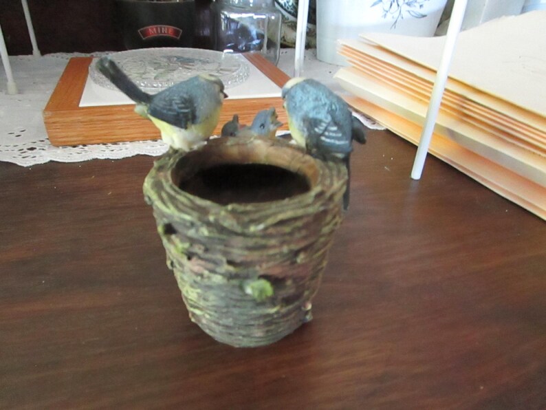 May include: A small ceramic birdhouse planter with a brown bark-like exterior and a green leafy accent. Four blue birds are perched on the rim of the planter.
