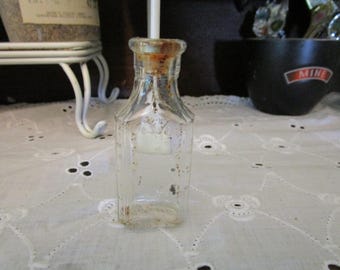 May include: A clear glass bottle with a cork stopper. The bottle has a textured surface and is slightly discolored.