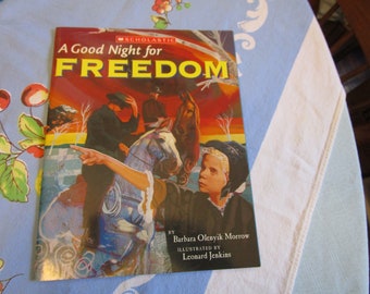 Könnte beinhalten: Ein Scholastic-Buch mit dem Titel "A Good Night for FREEDOM" von Barbara Olenyk Morrow, illustriert von Leonard Jenkins. Der Umschlag zeigt eine farbenfrohe Illustration eines Mädchens, das auf einem Pferd reitet, mit zwei Männern im Hintergrund.