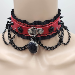 以下が含まれることがあります： 赤い革のバンド、黒いレースのトリム、銀色の金属のアクセント、黒い石のペンダントが付いた黒いチョーカーネックレス。チョーカーにはスパイクとチェーンが付いています。
